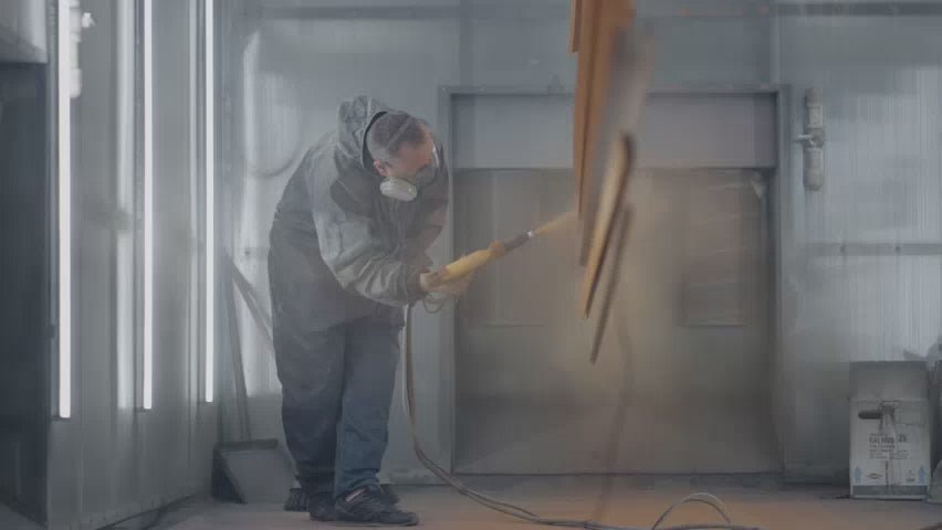 Man wearing protective suit spray painting sheet metal in manufacturing factory